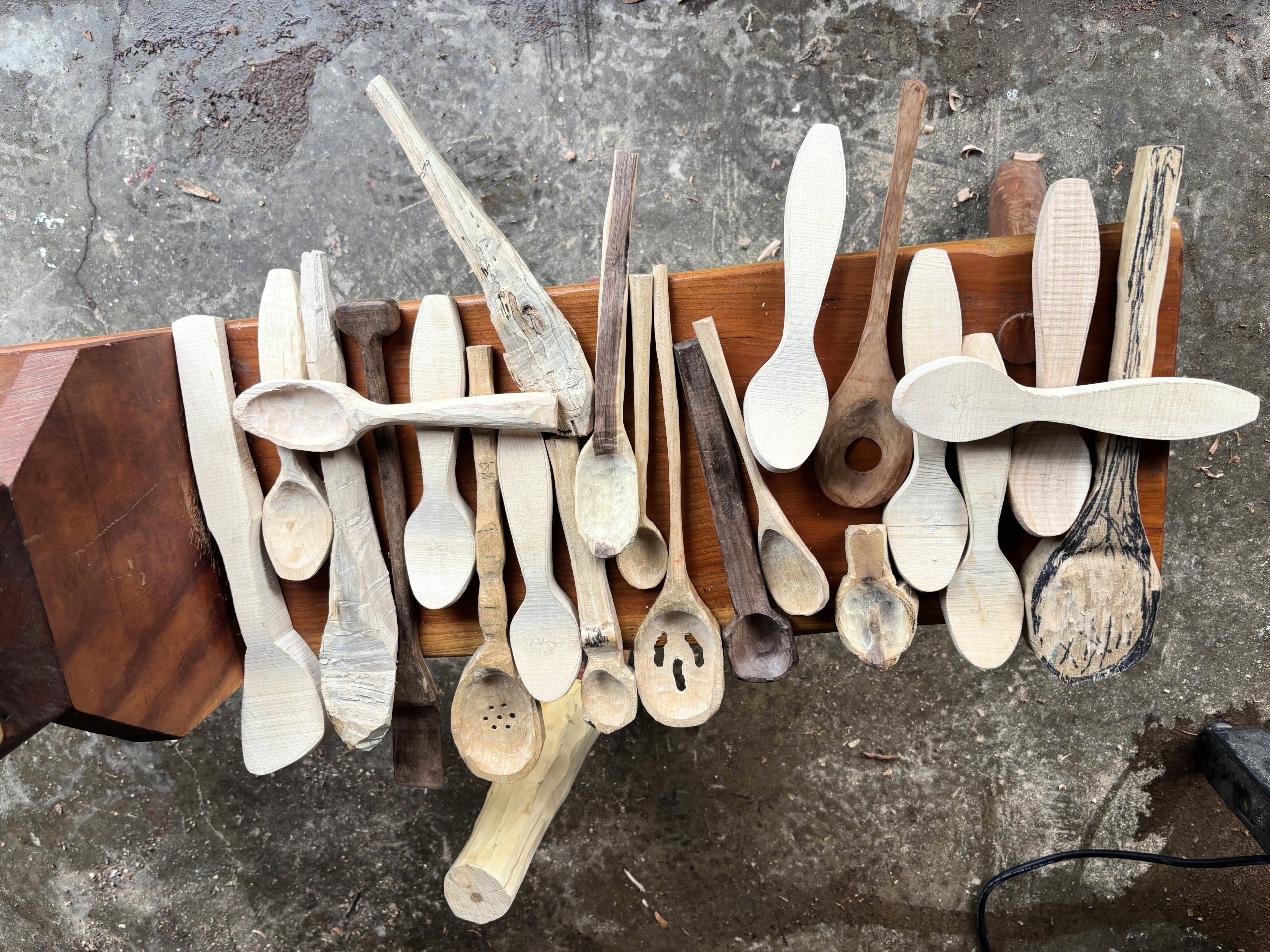 Collection of wooden spoons on a wooden board against a textured wall.