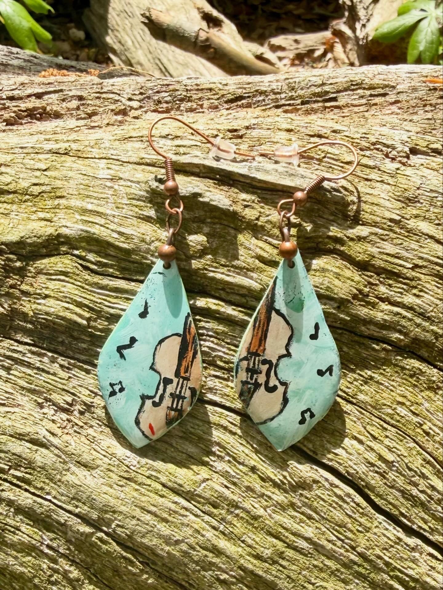 Teardrop-shaped earrings with fiddle design displayed on a wooden surface