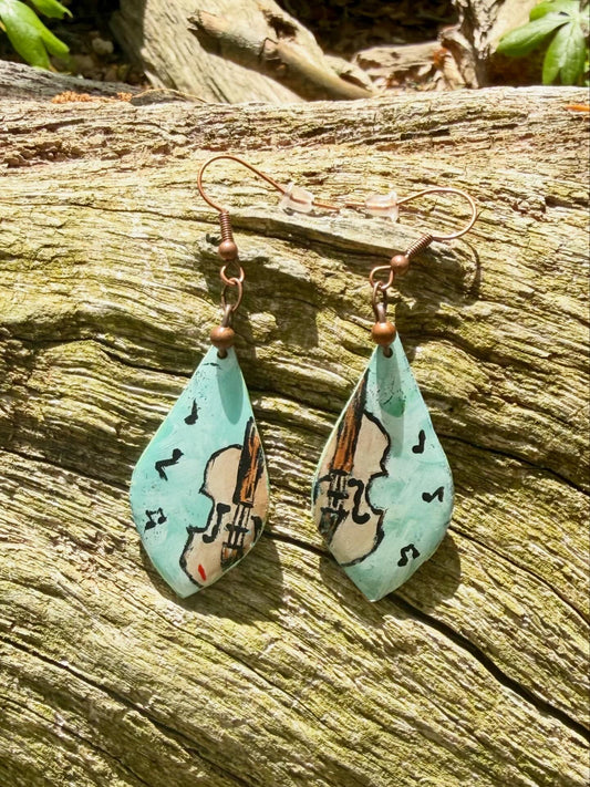 Teardrop-shaped earrings with fiddle design displayed on a wooden surface
