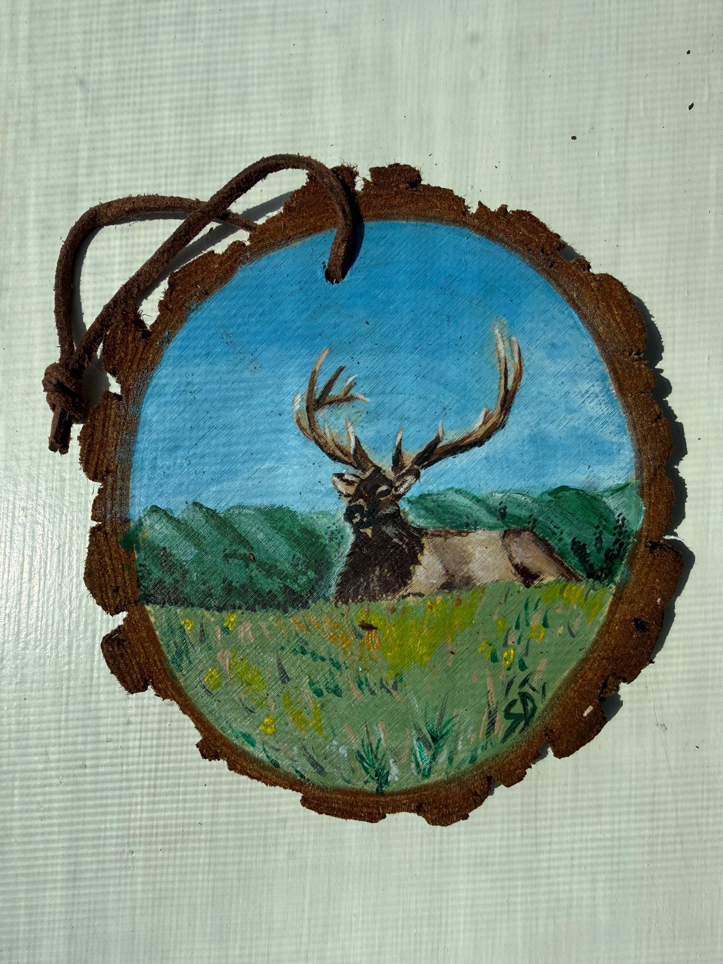 Wooden ornament with a painted design of an elk and landscape