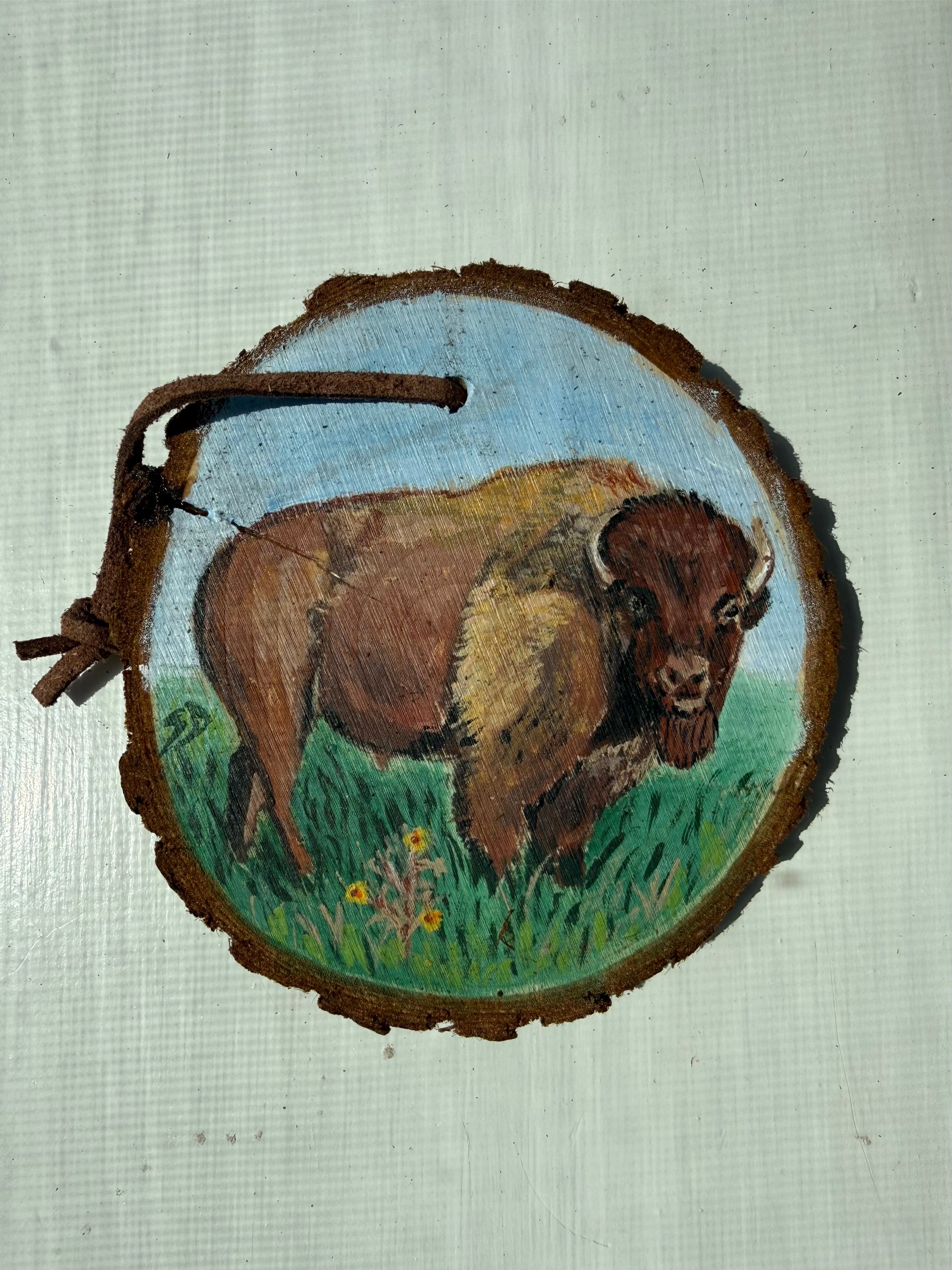 Painting of a bison on a wooden ornament with a natural background