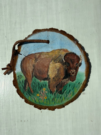 Painting of a bison on a wooden ornament with a natural background