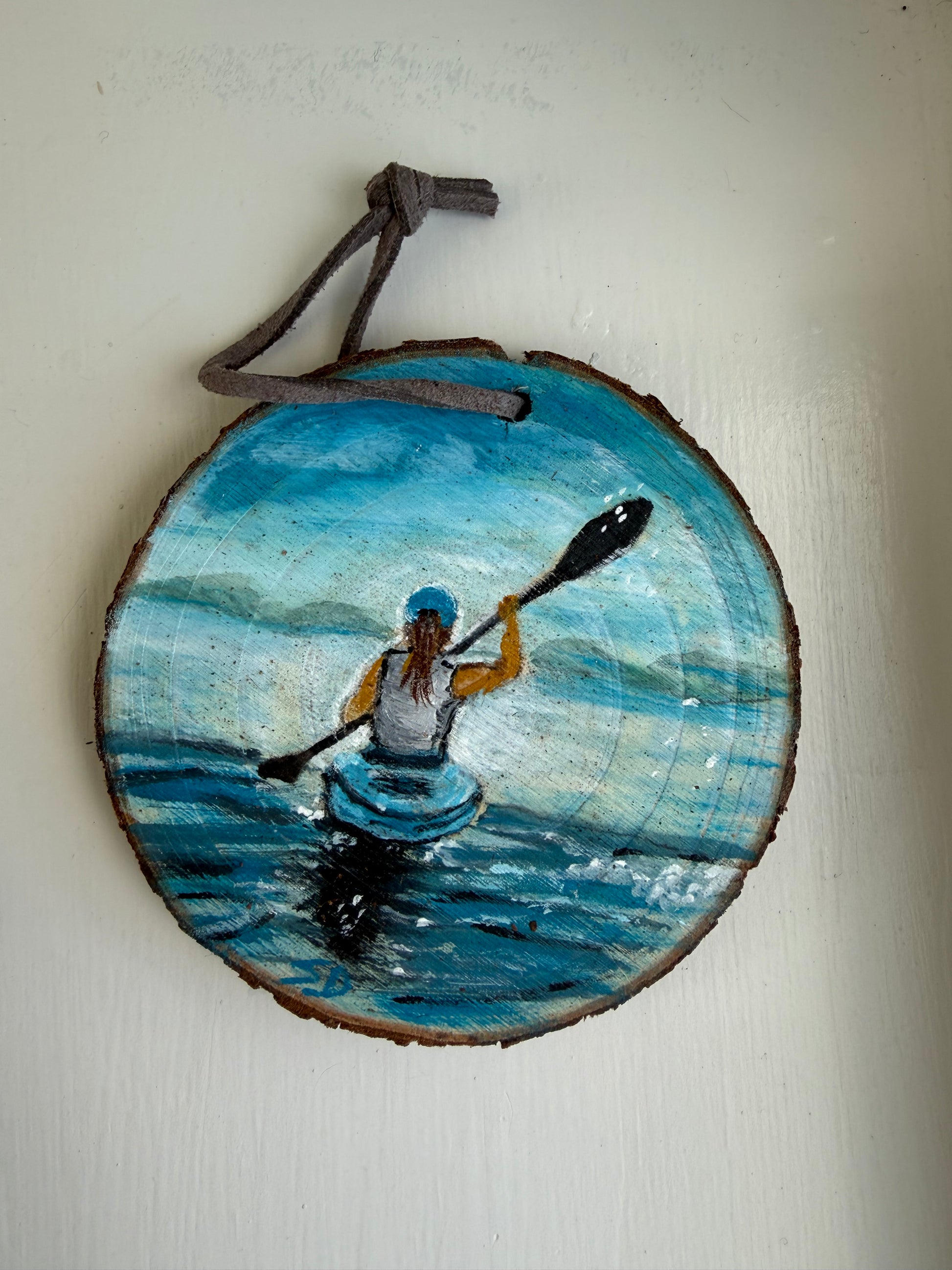 Wooden ornament with a painted scene of a person in a kayak on a blue wave