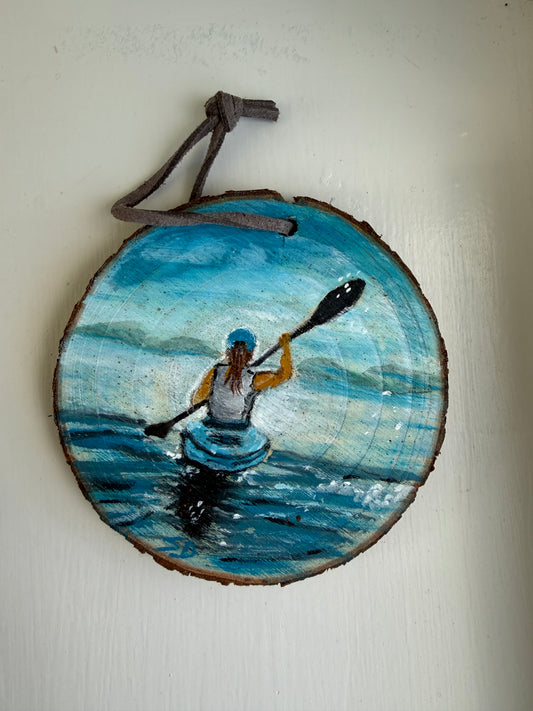 Wooden ornament with a painted scene of a person in a kayak on a blue wave