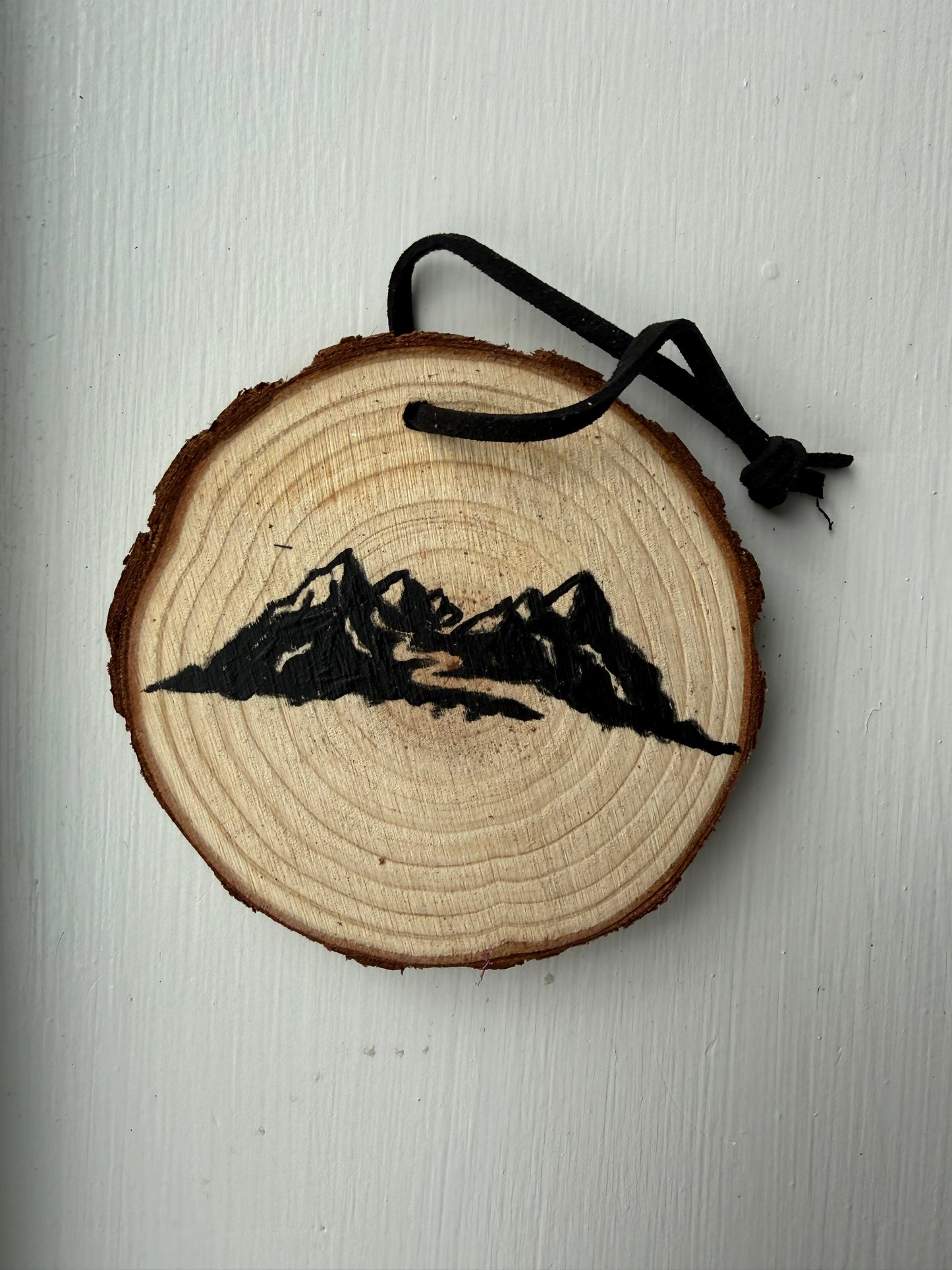 Wooden ornament with a painted mountain design on it