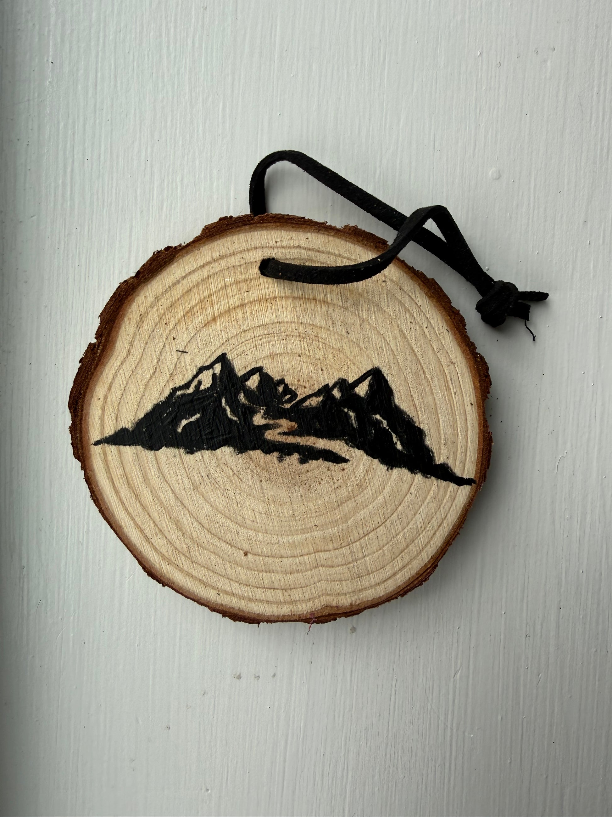 Wooden ornament with a painted mountain design on it