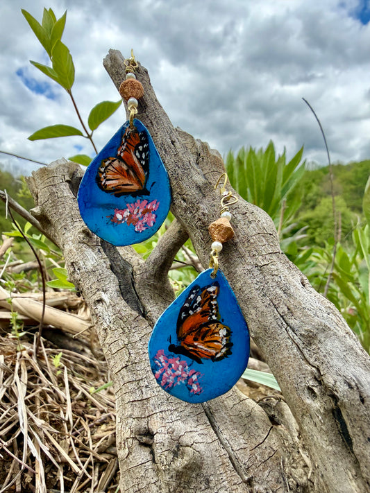 Teardrop-shaped earrings with butterfly design on a branch outdoors