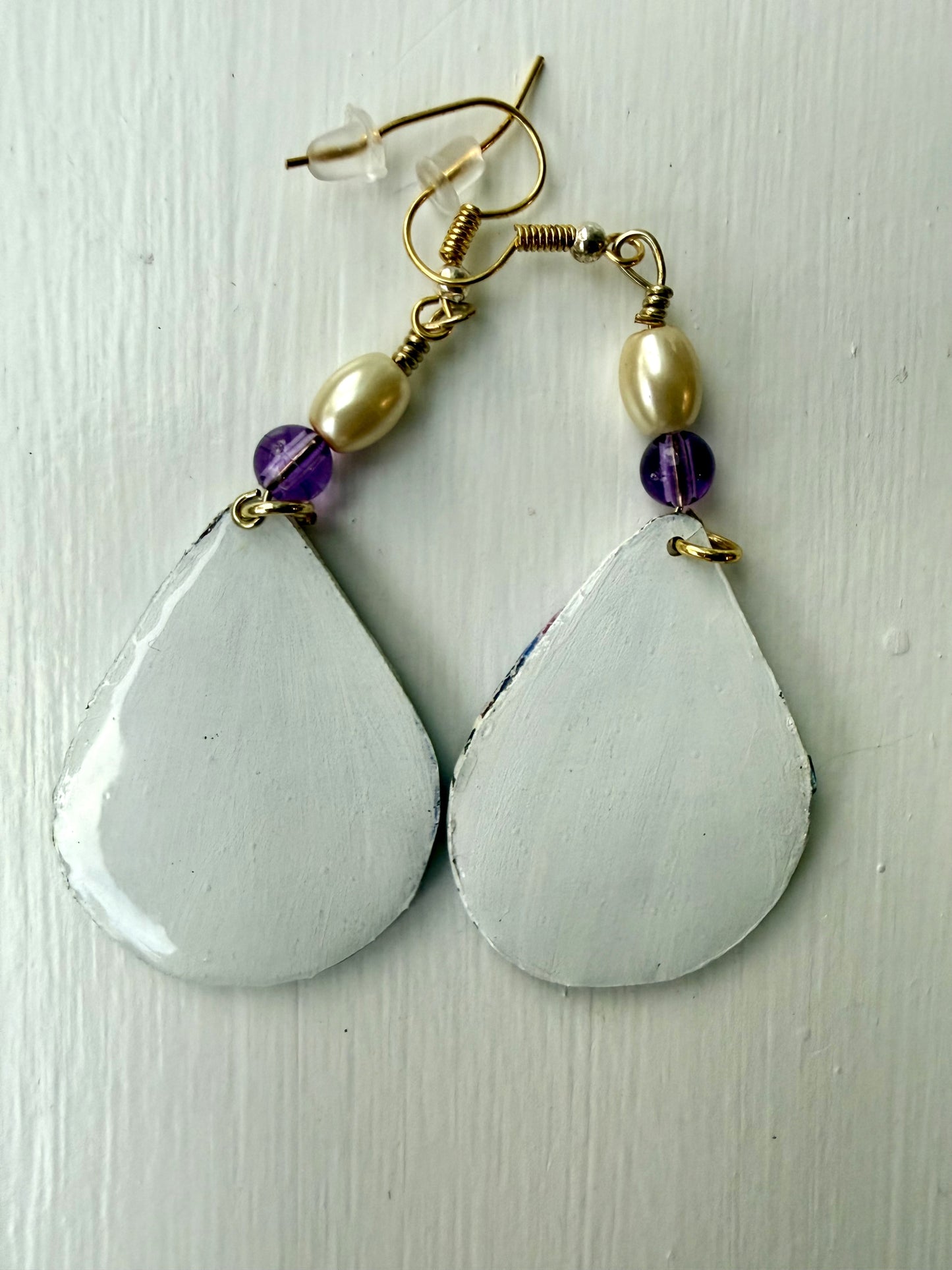 White teardrop-shaped earrings with glass pearl and purple beads on a white backround