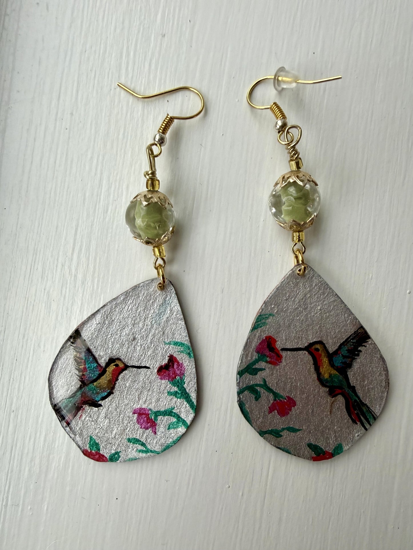 Teardrop-shaped earrings with hummingbird design on a light wooden surface