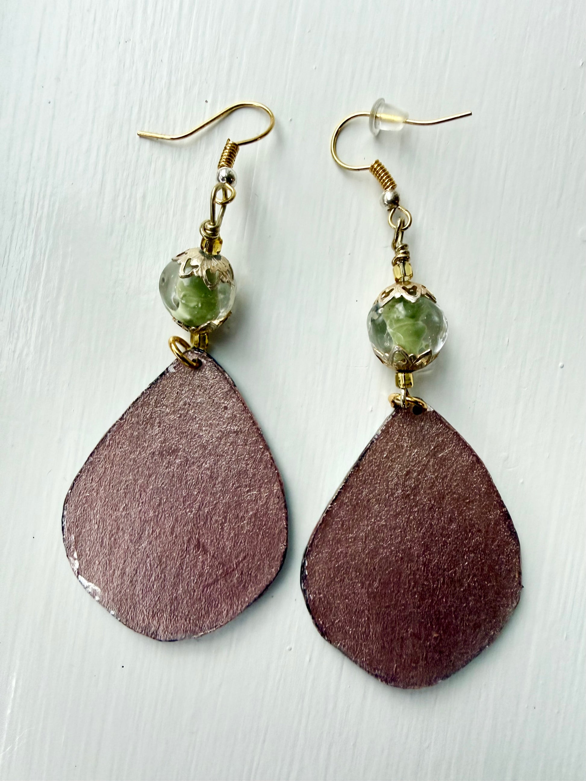 Bronze teardrop-shaped earrings on a light wooden surface