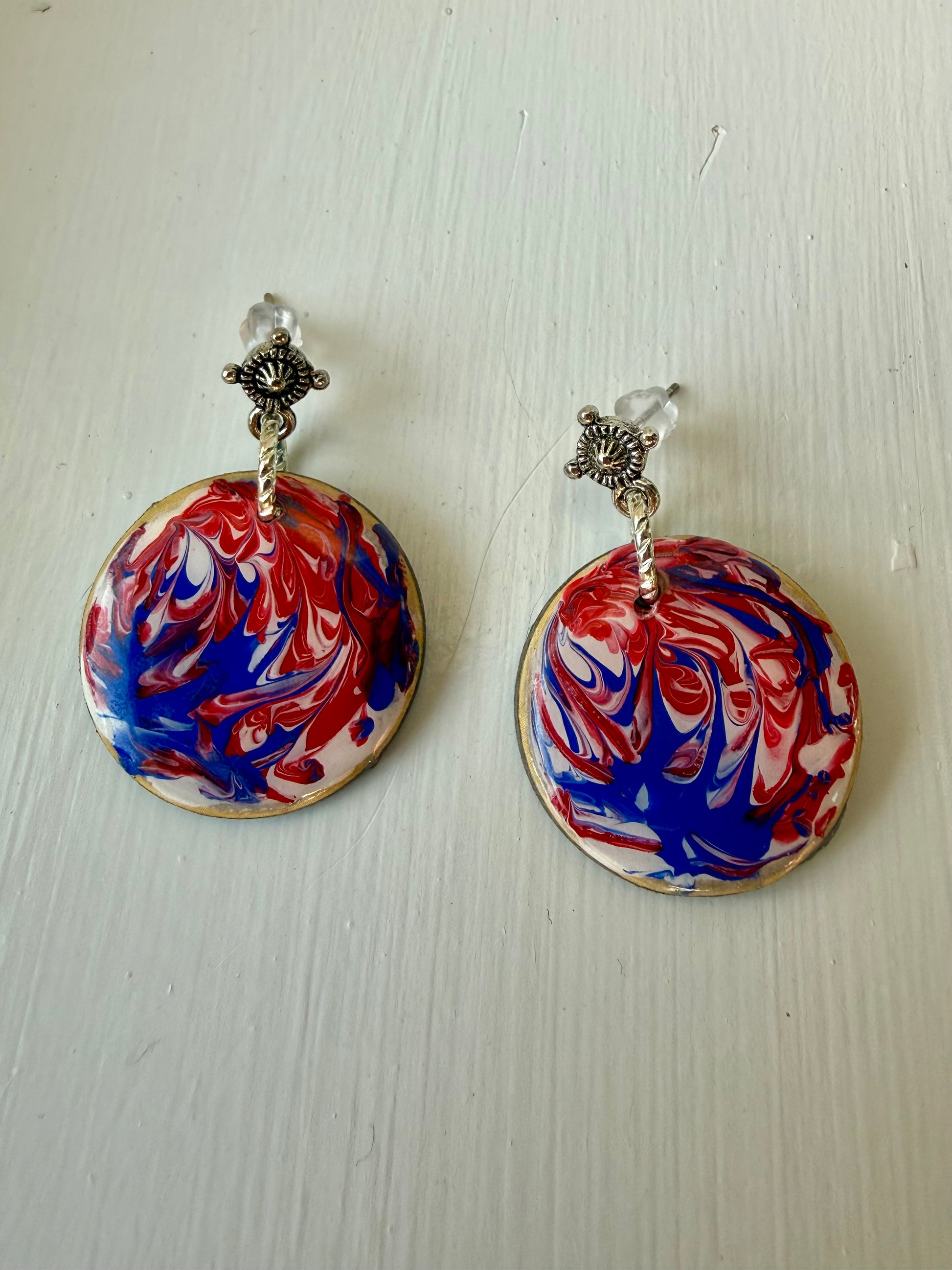 Pair of earrings with red, white, and blue marbled design on a light wooden surface.
