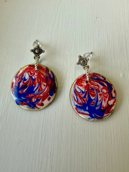 Pair of earrings with red, white, and blue marbled design on a light wooden surface.