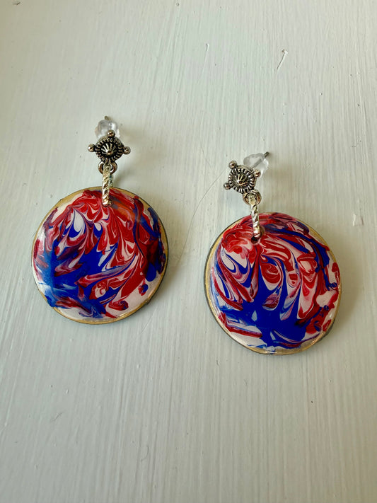 Pair of earrings with red, white, and blue marbled design on a light wooden surface.