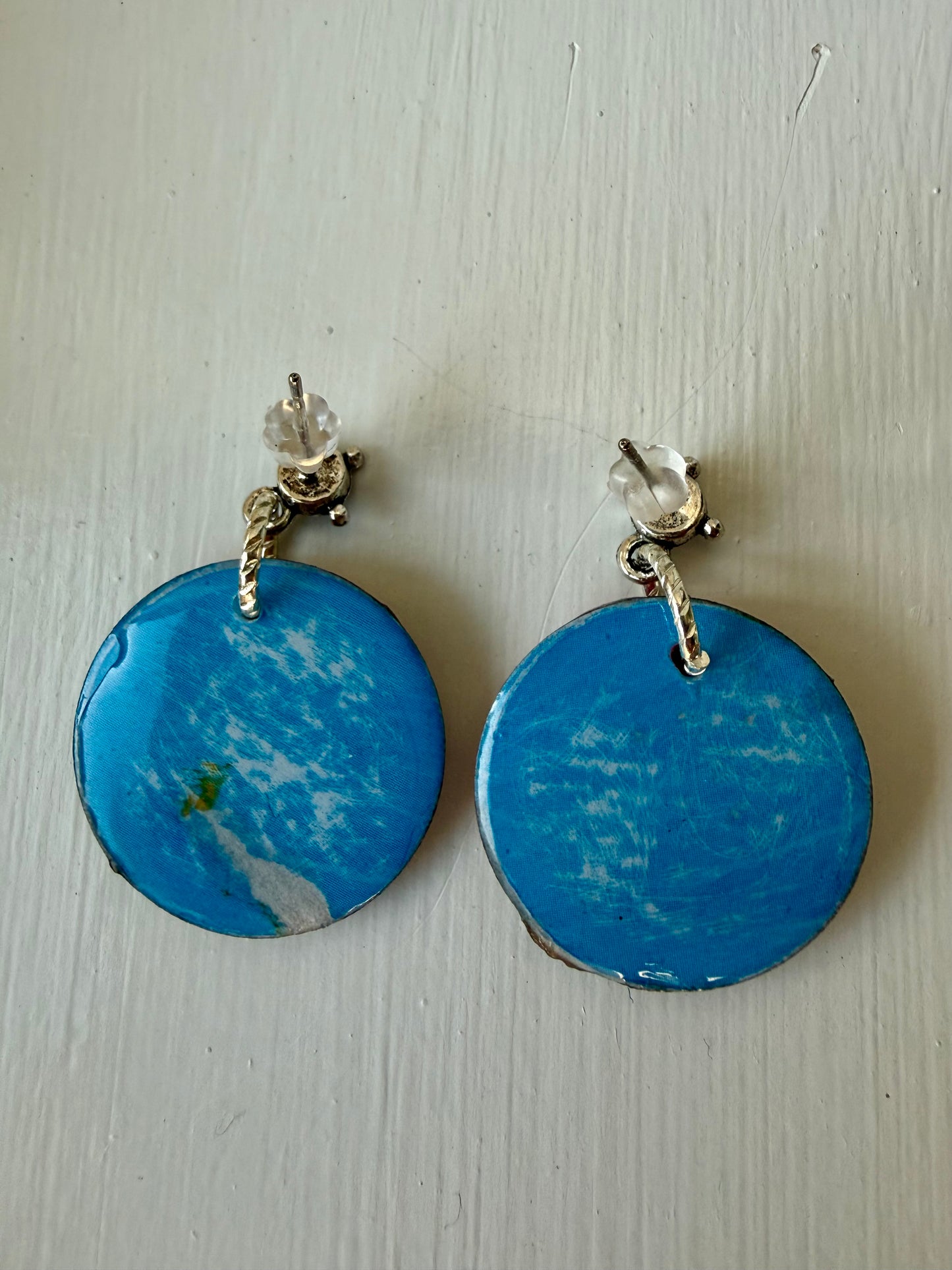 Blue and white circular earrings with silver accents on a light wooden surface.