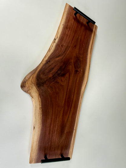 Wooden charcuterie board with black handles and a natural edge on a white background