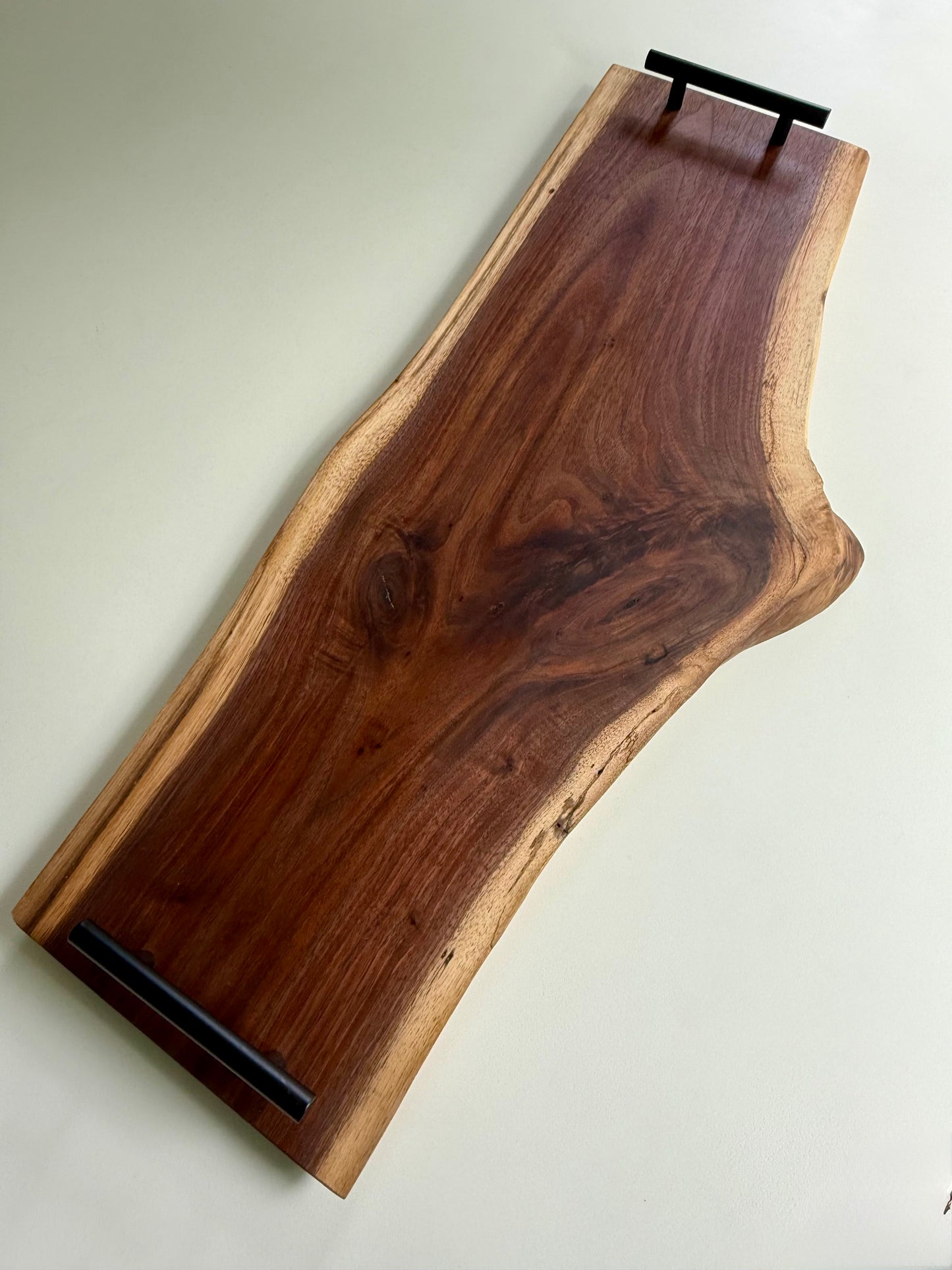 Wooden charcuterie board with black handles and a natural edge on a white background