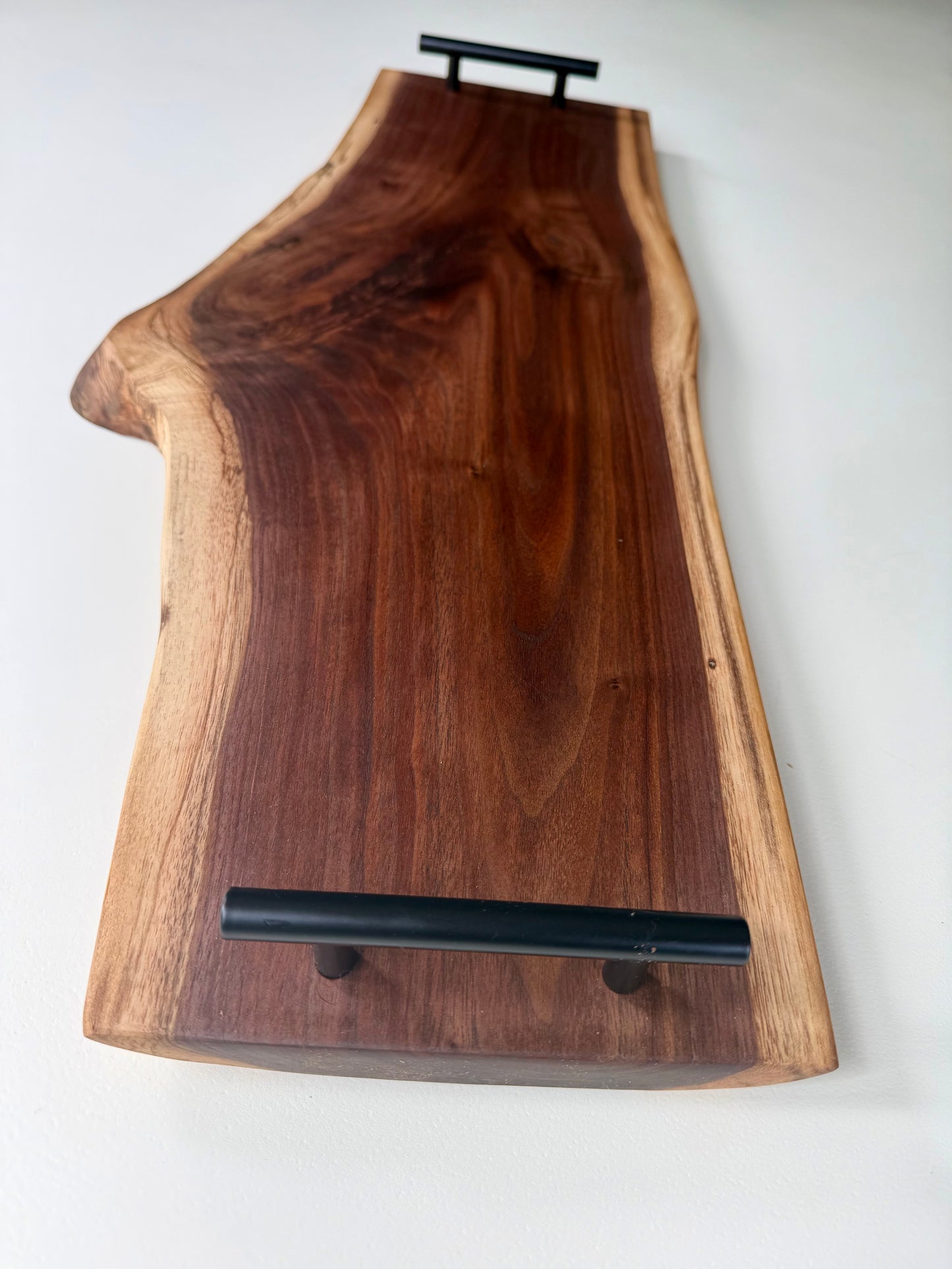 Wooden charcuterie board with black handles and a natural edge on a white background