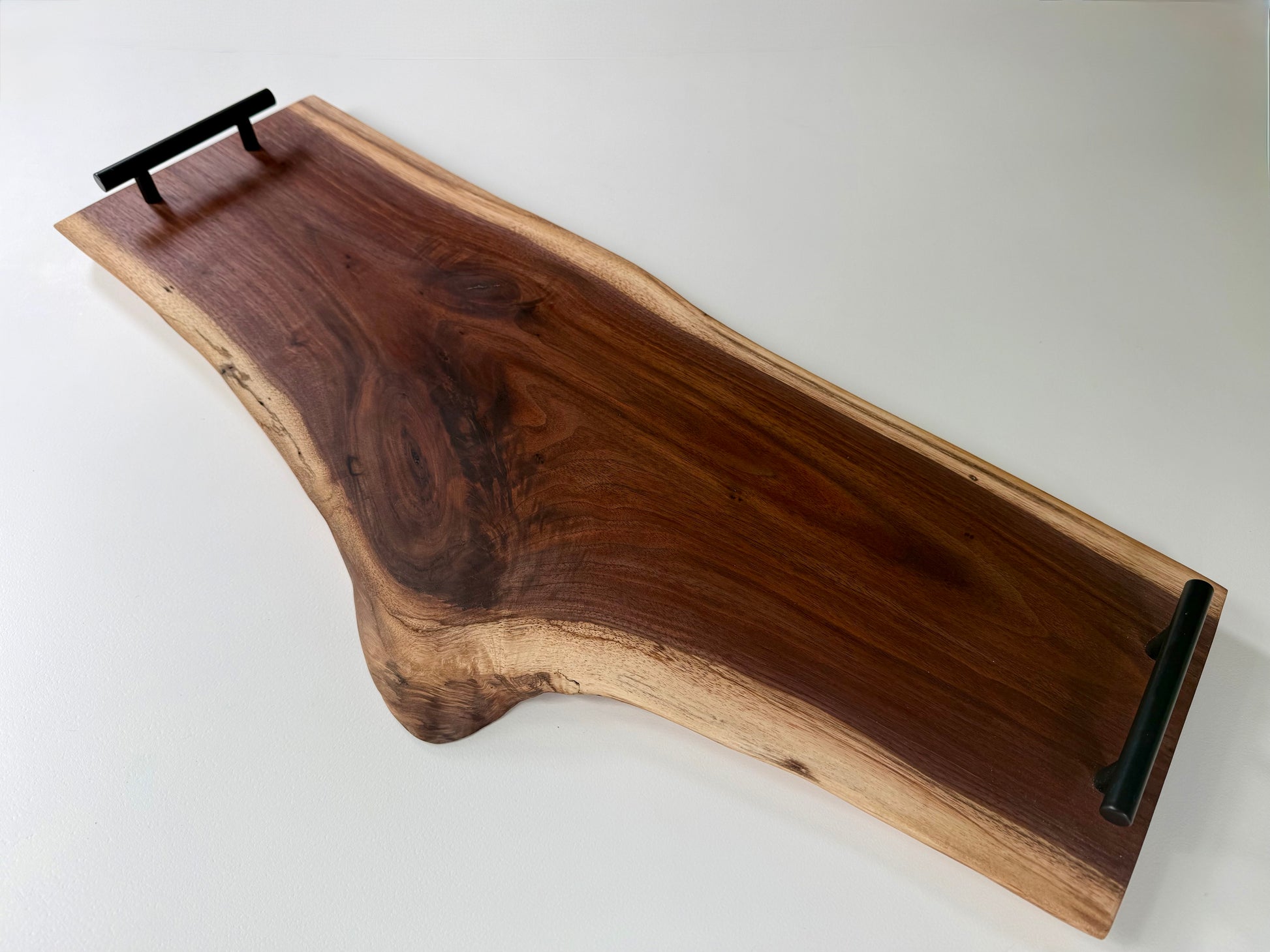 Wooden charcuterie board with black handles and a natural edge on a white background