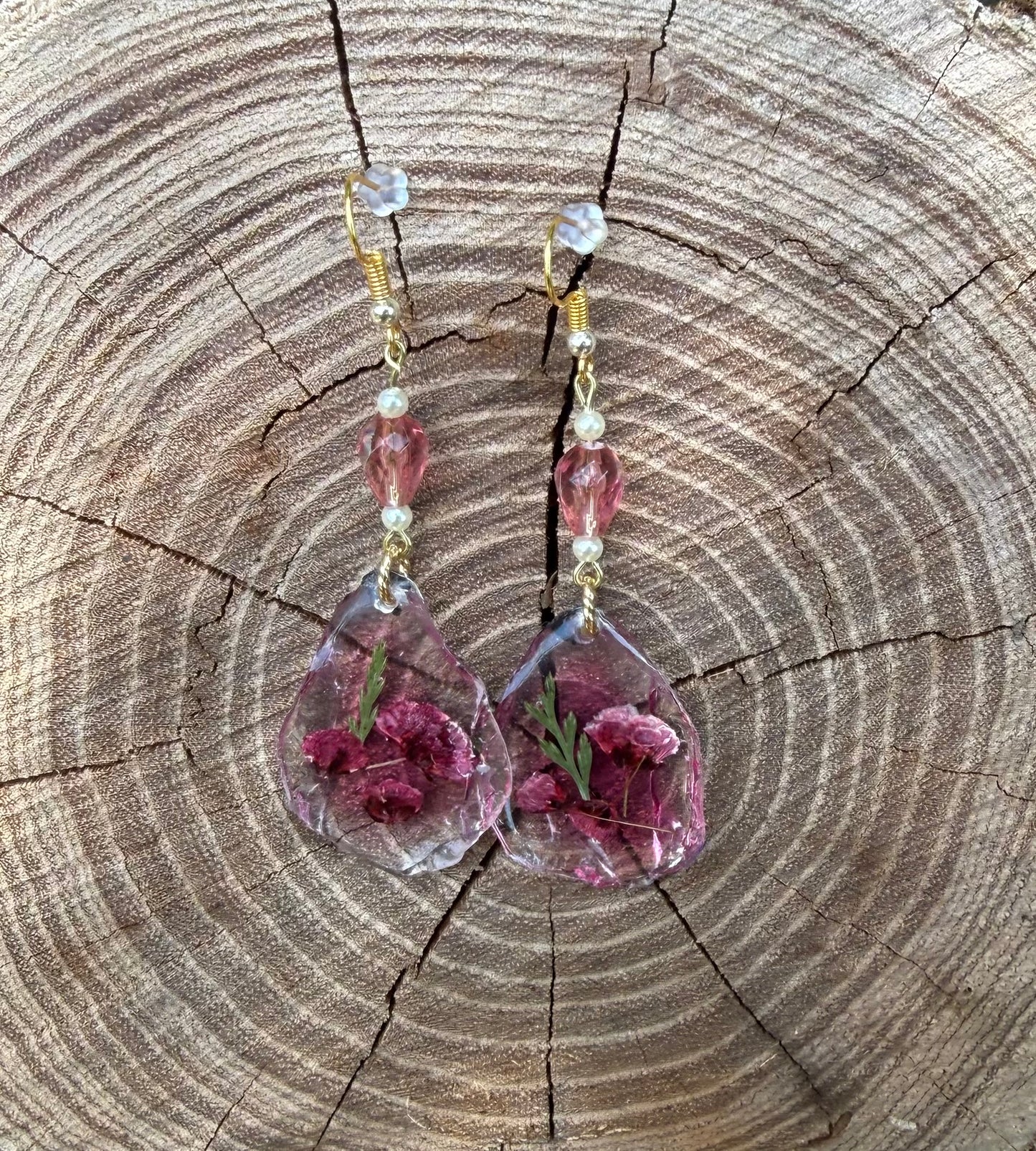 Teardrop earrings with dried flowers encased inside, displayed on stump