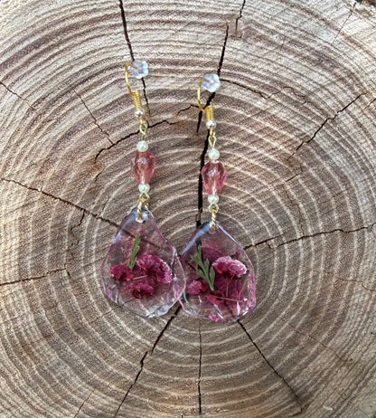 Teardrop earrings with dried flowers encased inside, displayed on stump