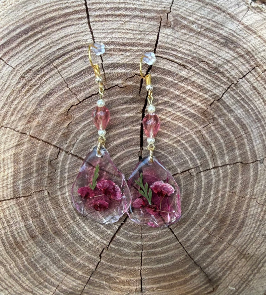 Teardrop earrings with dried flowers encased inside, displayed on stump