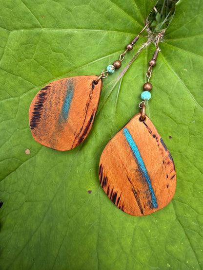 Wooden earrings with blue accents on a green leaf