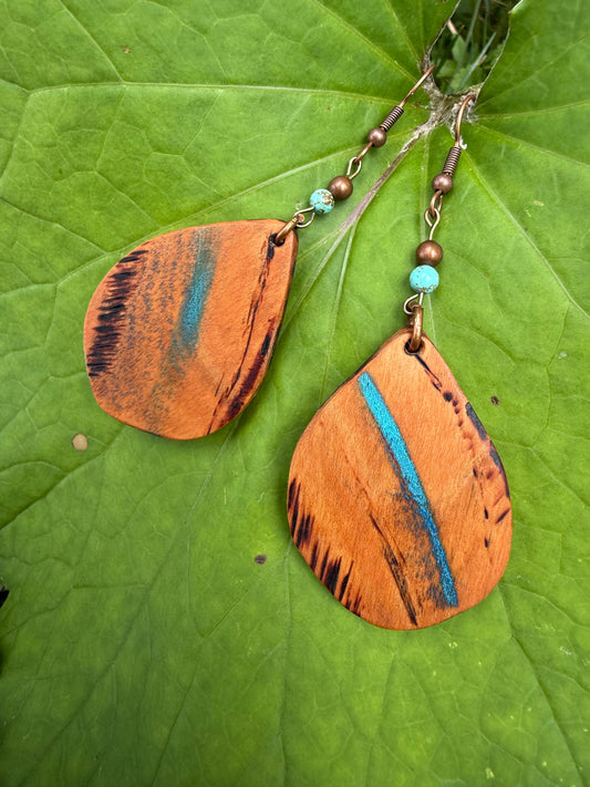 Wooden earrings with blue accents on a green leaf