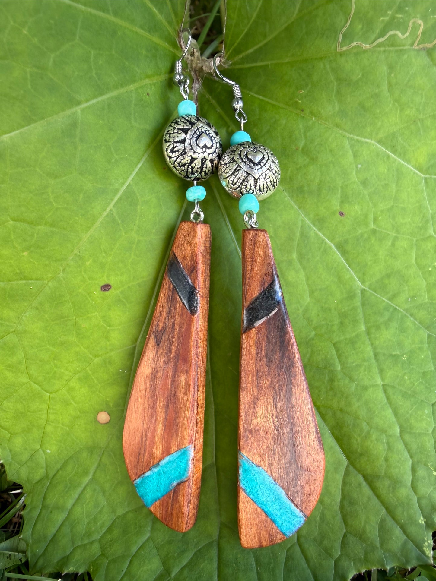 Wooden earrings with turquoise accents and silver beads on a green leaf background