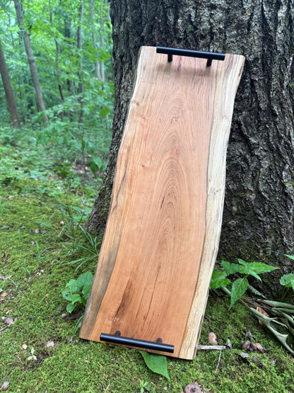 Wooden cutting board with black handles leaning against a tree