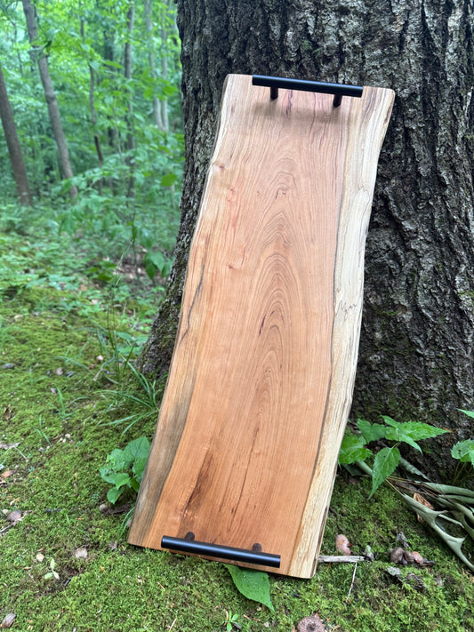Wooden cutting board with black handles leaning against a tree