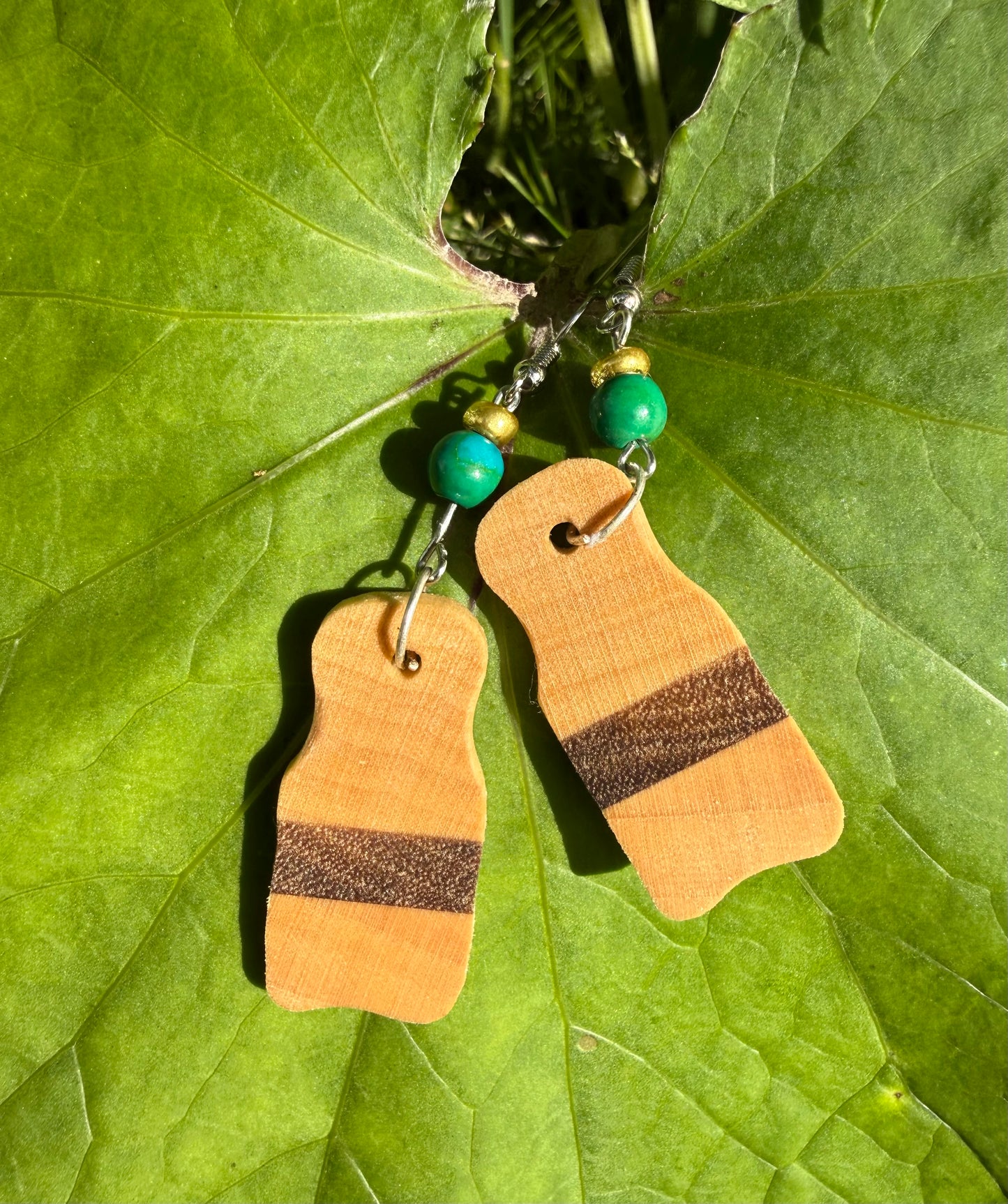 Wooden earrings with brown stripes on a green leaf background