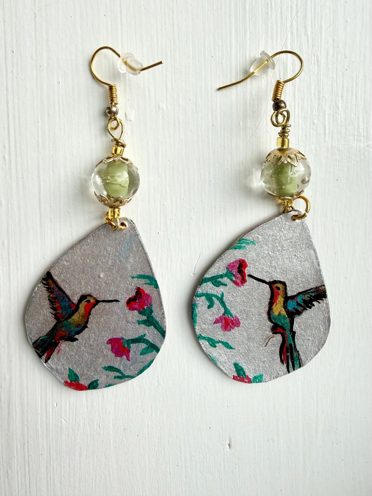 Teardrop-shaped earrings with hummingbird design on a light wooden surface