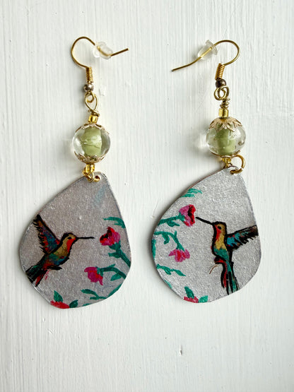 Teardrop-shaped earrings with hummingbird design on a light wooden surface