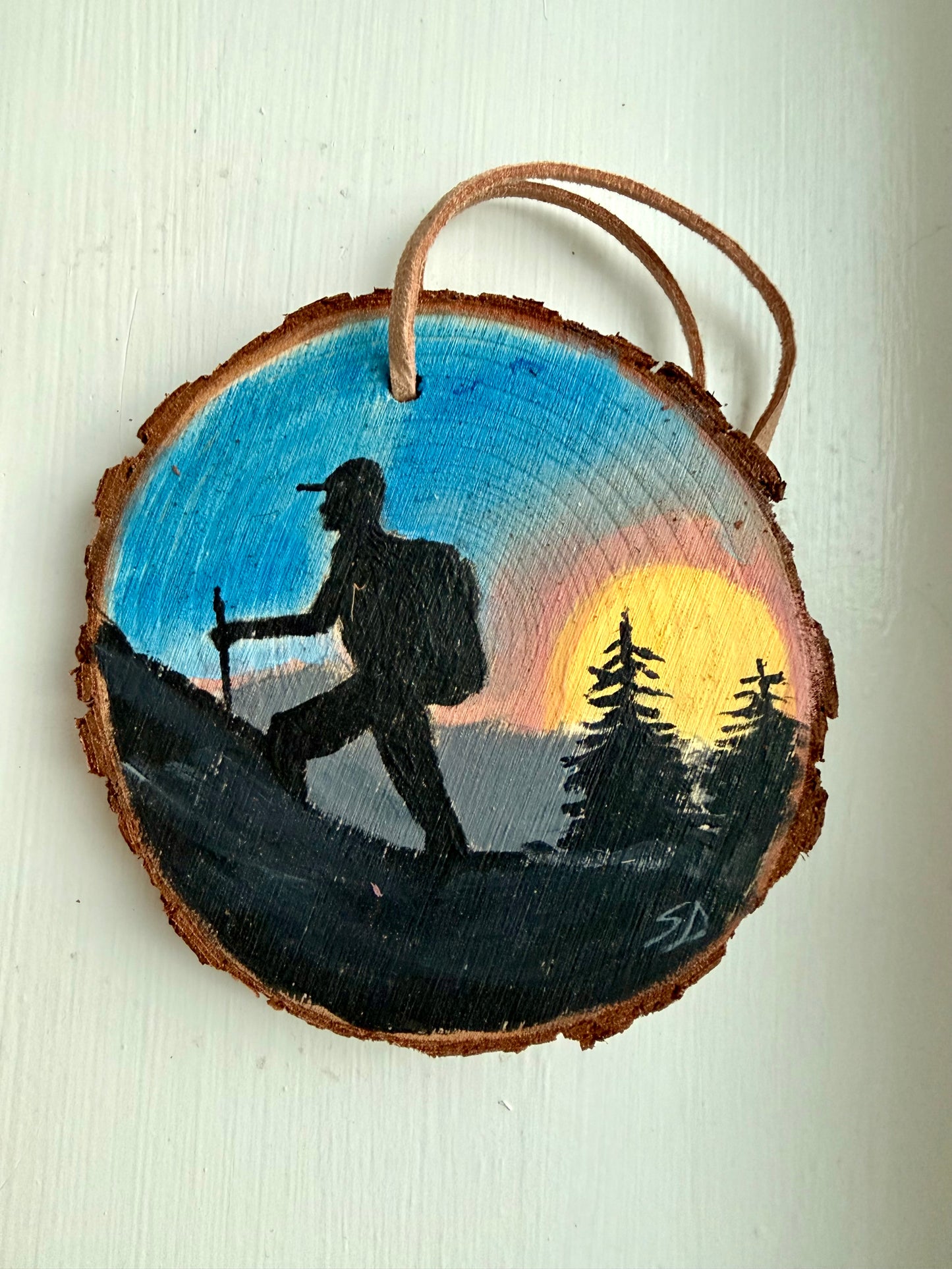 Wooden ornament with a painted design of a hiker and sunset