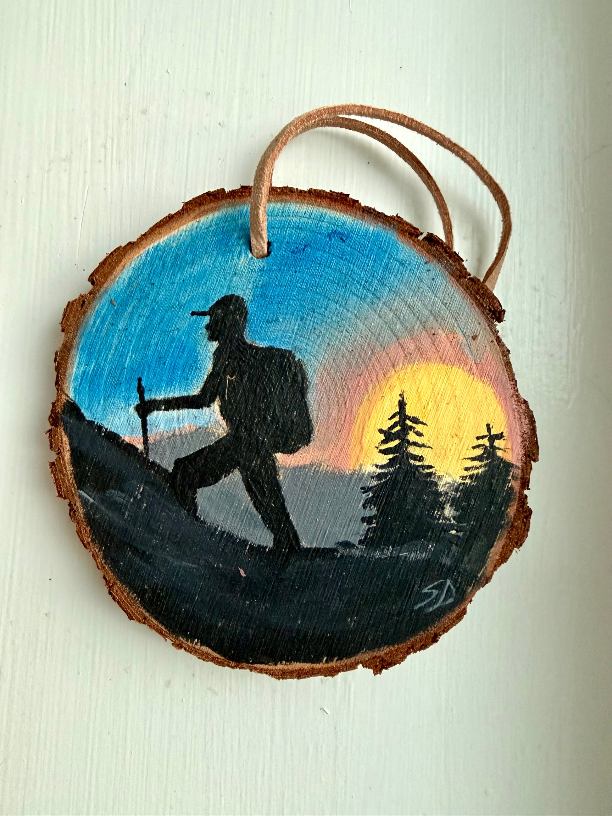 Wooden ornament with a painted design of a hiker and sunset