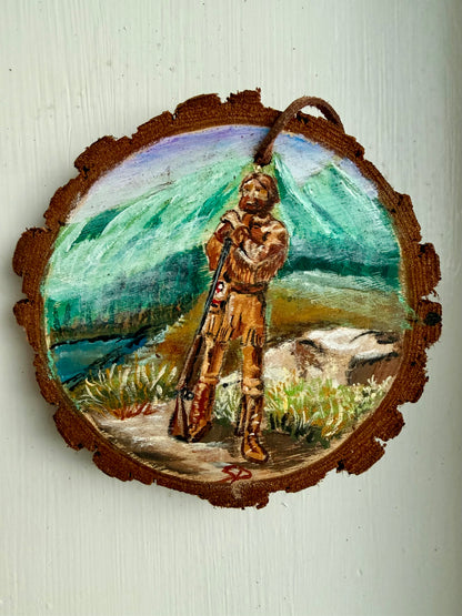 Wooden ornament featuring a mountain man design with a mountain landscape in the background