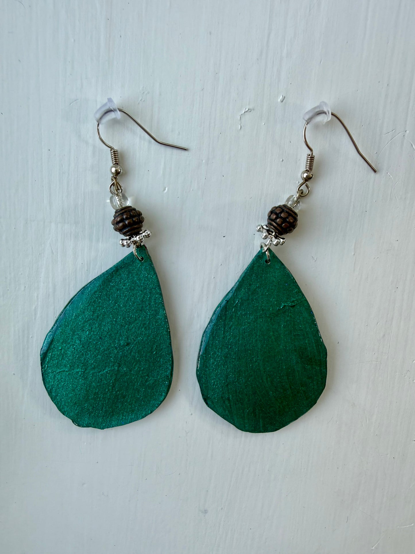 A pair of teardrop-shaped dangle earrings with teal back, hanging on silver coated metal hooks.