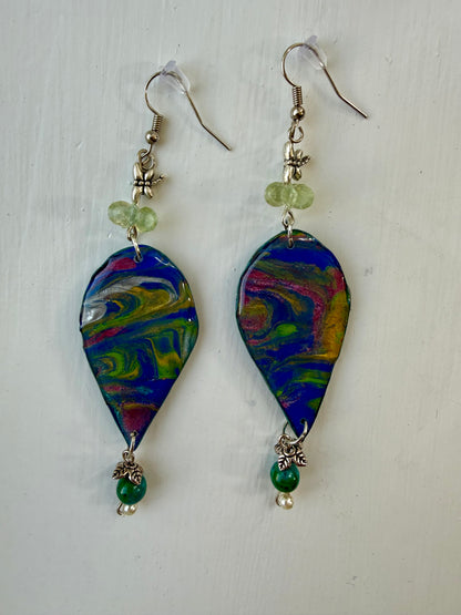 A pair of teardrop-shaped dangle earrings with colorful marbled paint designs in blue, green, yellow, pink, and white, hanging on silver coated metal hooks.