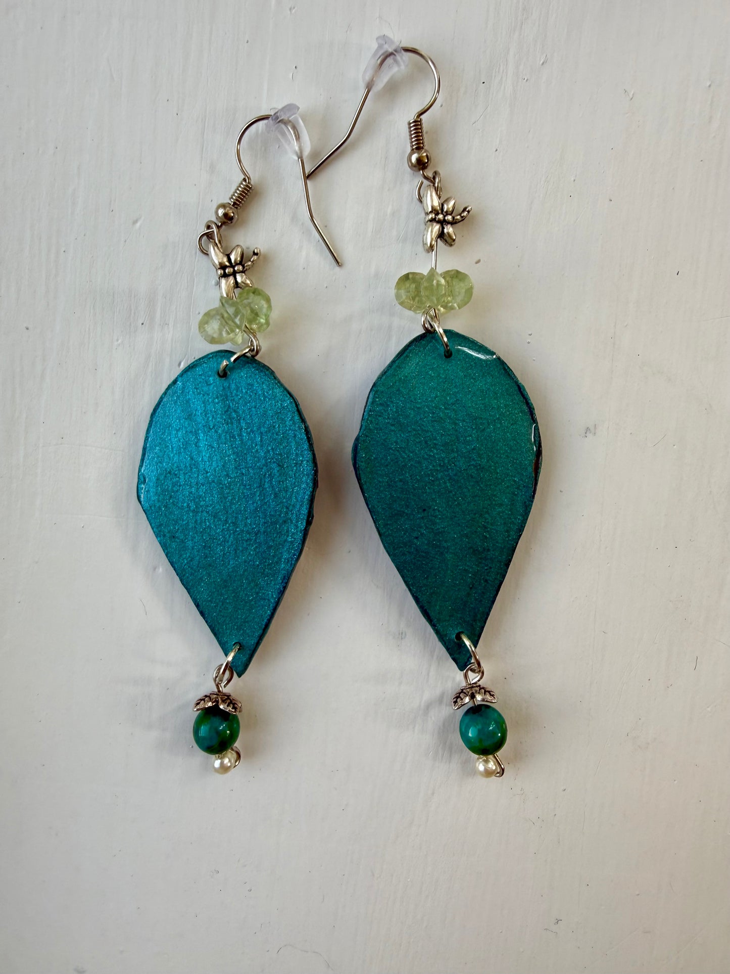 A pair of teardrop-shaped dangle earrings with blue back, hanging on silver coated metal hooks.