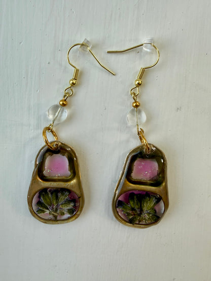 A pair of gold-tone dangle earrings with blue topaz beads and pink and floral inlay, displayed on a white textured background.
