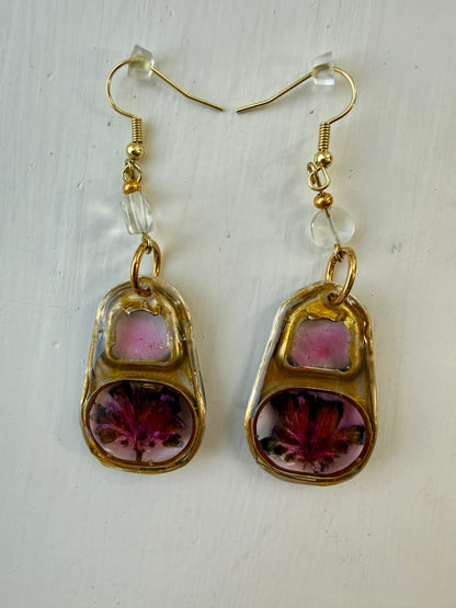 A pair of gold-tone dangle earrings with blue topaz beads and pink and floral inlay, displayed on a white textured background.