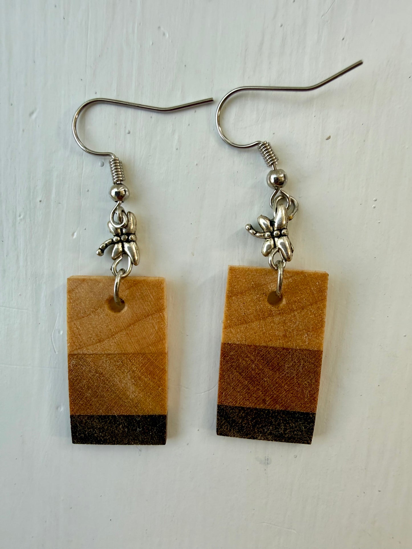 Two rectangular drop earrings featuring three horizontal wood-patterned stripes in light tan, medium brown, and dark charcoal. Each earring hangs from a silver-coated metal ear hook with a small silver-coated metal dragonfly bead.