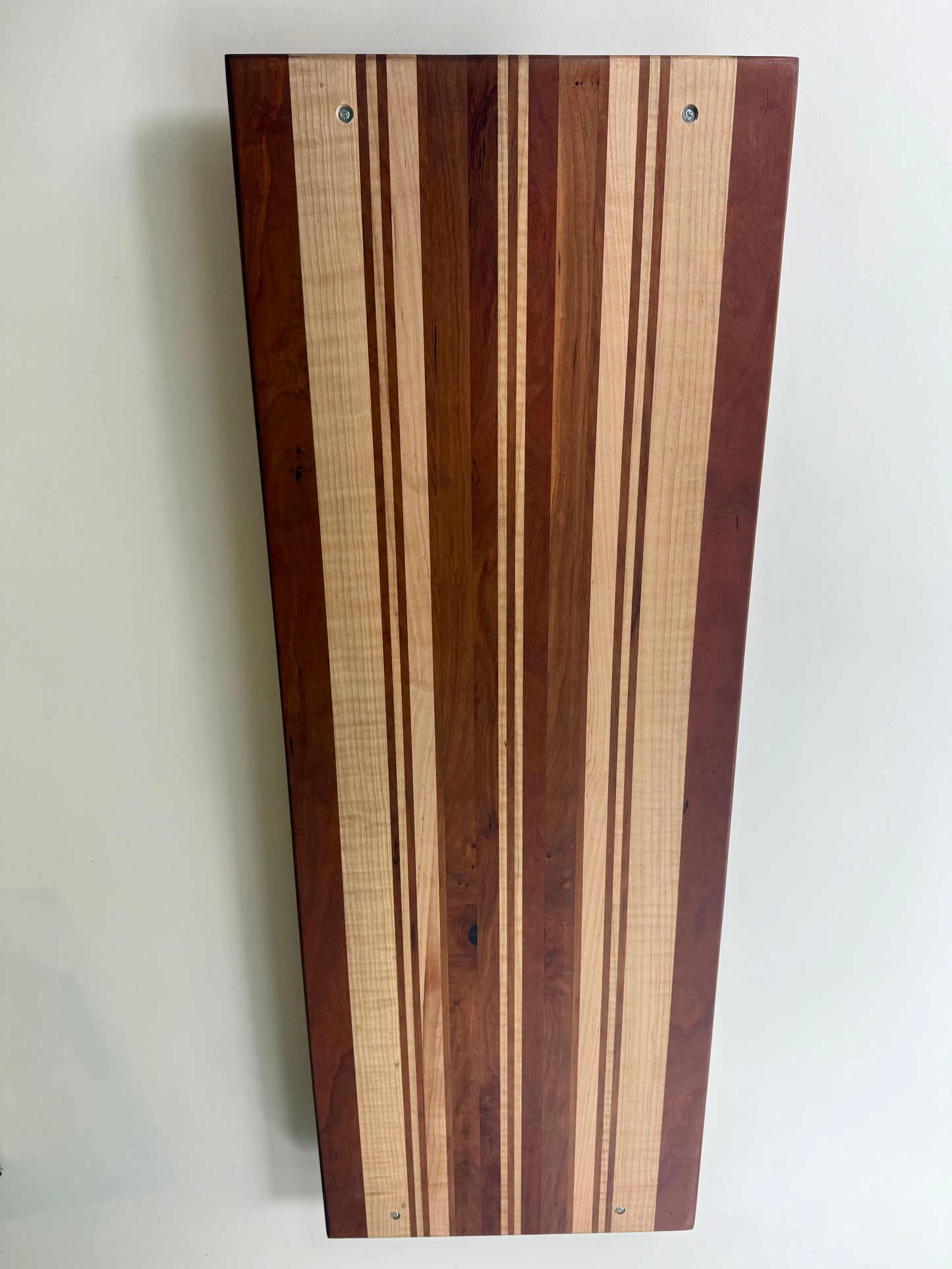 The back of a rectangular wooden serving board with a striped pattern of light and dark wood tones
